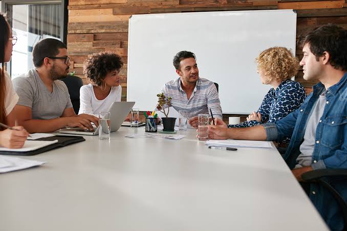Project team discussing roles around a conference table in front of a whiteboard