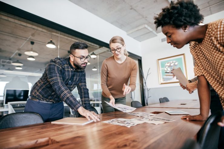 Project manager and team reviewing printed project plans spread across a conference table