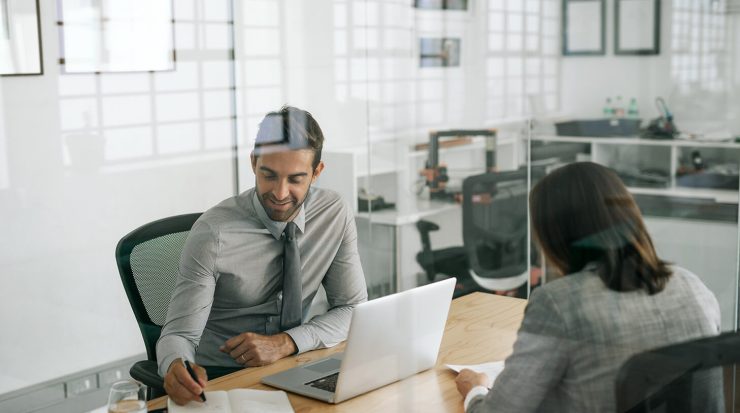 Hiring manager interviewing a project coordinator candidate at a desk with a laptop