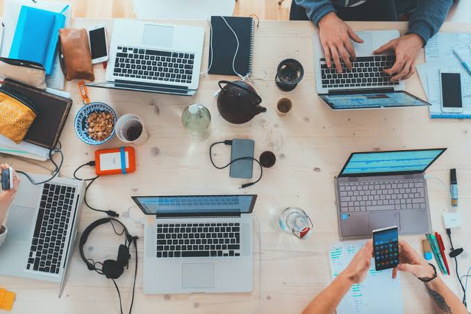 Overhead view of a project team working on laptops and phones around a shared wooden desk