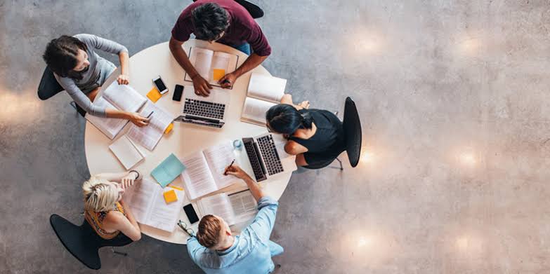 Overhead view of a project team planning around a round table with laptops, notebooks and sticky notes