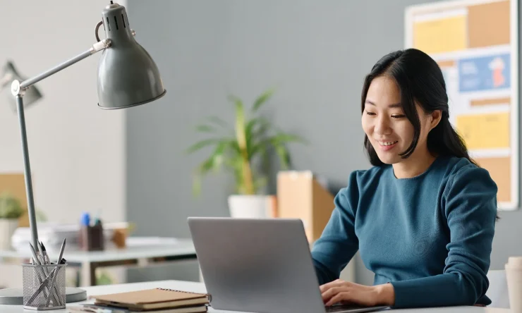 Executive research assistant smiling while working on a laptop at a bright office desk